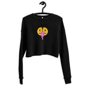 May include: Black cropped sweatshirt with long sleeves, suspended from a black hanger. The sweatshirt displays the word "PLURNT" above a yellow smiley face with a pink, melting design.