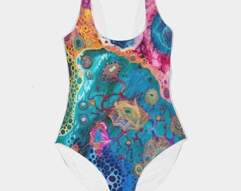 May include: One-piece swimsuit with a vibrant, abstract design. The swimsuit features a colorful pattern with shades of blue, pink, yellow, and orange. The straps and the bottom are white. The design has a unique, artistic look.
