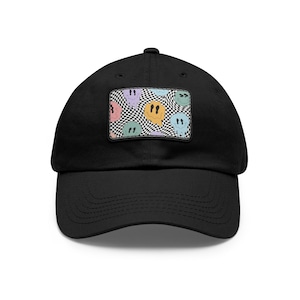 Puede incluir: Una gorra de béisbol negra con un patrón de cuadros y caras sonrientes de colores en la parte delantera.