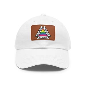Puede incluir: Gorra de béisbol blanca con un parche de cuero marrón con el texto "PSYCHEDELIC RESEARCH VOLUNTEER" en un diseño triangular con colores arcoíris. La gorra tiene una visera curva y un cierre de correa de tela.