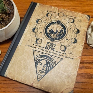 May include: A journal with a vintage design, featuring a celestial design with a moon and phases, and the text "EXO NYM A JOURNAL OF INTERPLANETARY EXPLORATION." The cover also includes a triangular portrait of a person in a space helmet.