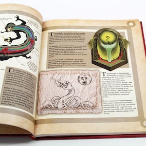 May include: An open book with illustrations of a basilisk, a mythical creature. The left page features a diagram of the basilisk's anatomy, while the right page shows a drawing of the creature and text. The book has a red cover.