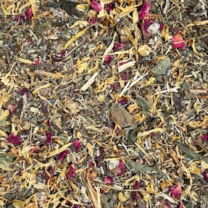 May include: Close-up of a mix of dried herbs and flowers. The blend includes small, dried rose petals, yellow petals, and green leaves, creating a textured, natural appearance. The overall color palette is earthy, with hints of red and yellow.