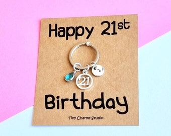 May include: A card with the text "Happy 21st Birthday" and a silver keychain with a turquoise gem, a silver charm with the number 21, and a silver initial charm.