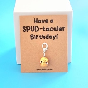 May include: A brown card with the text "Have a SPUD-tacular Birthday!" and a small, brown, potato-shaped charm with a white face and a silver keychain attached.