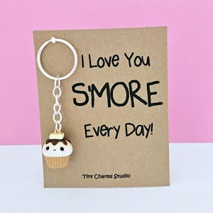 May include: A brown card with the text "I love you s'more every day!" and a small keychain charm shaped like a s'more with a smiling face. The charm is attached to a silver key ring.