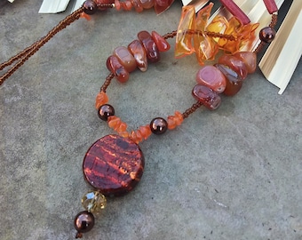 May include: A multi-strand necklace with carnelian, amber, and brown beads. The necklace features a large, round, red and brown pendant.