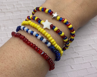 May include: Five beaded bracelets in red, yellow, blue, and white. Two bracelets have star charms. The bracelets are made of small, colorful beads strung together, creating a vibrant and playful accessory.