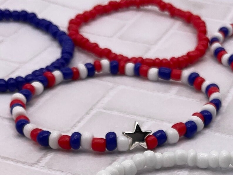 May include: Several beaded bracelets in red, white, and blue. One bracelet features a silver star charm. The bracelets are made of small, round beads, and are likely elasticated for easy wear. Patriotic theme.