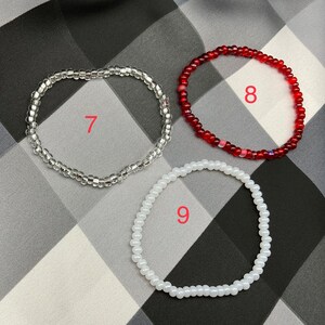 May include: Three beaded bracelets in different colors and sizes. The bracelet on the left is clear, the middle bracelet is red, and the bracelet on the right is white. The bracelets are numbered 7, 8, and 9.