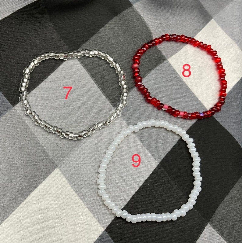 May include: Three beaded bracelets in different colors and sizes. The bracelet on the left is clear, the middle bracelet is red, and the bracelet on the right is white. The bracelets are numbered 7, 8, and 9.
