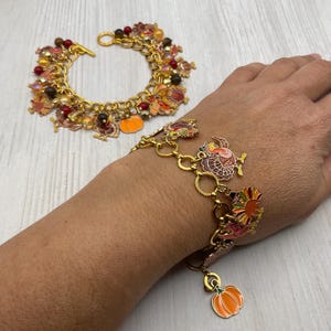 May include: Two gold-tone charm bracelets featuring colorful enamel turkey and pumpkin charms, interspersed with red, brown, and yellow beads. The bracelets have a toggle clasp closure and are designed with a link chain construction.