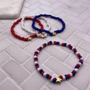 May include: Red, white, and blue beaded bracelets with gold star charms. The bracelets are made of small, round beads and are arranged in a patriotic color scheme. The bracelets are a perfect accessory for any occasion.