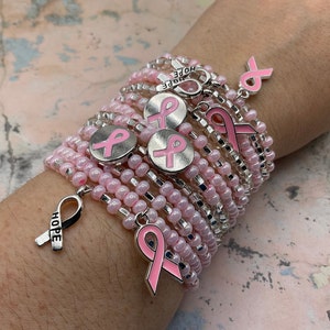 May include: A stack of pink and silver beaded bracelets with pink ribbon charms. The charms say "HOPE" and feature a pink ribbon design.