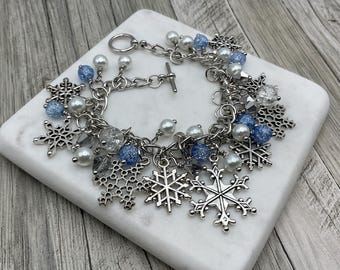 May include: A silver charm bracelet with snowflake charms, white pearls, and blue glass beads.