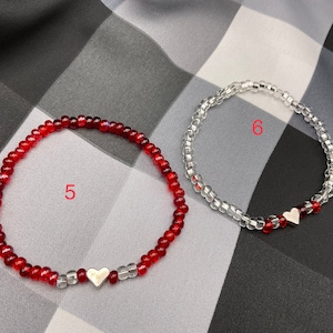 May include: Two beaded bracelets with silver heart charms. One bracelet is red and the other is clear.