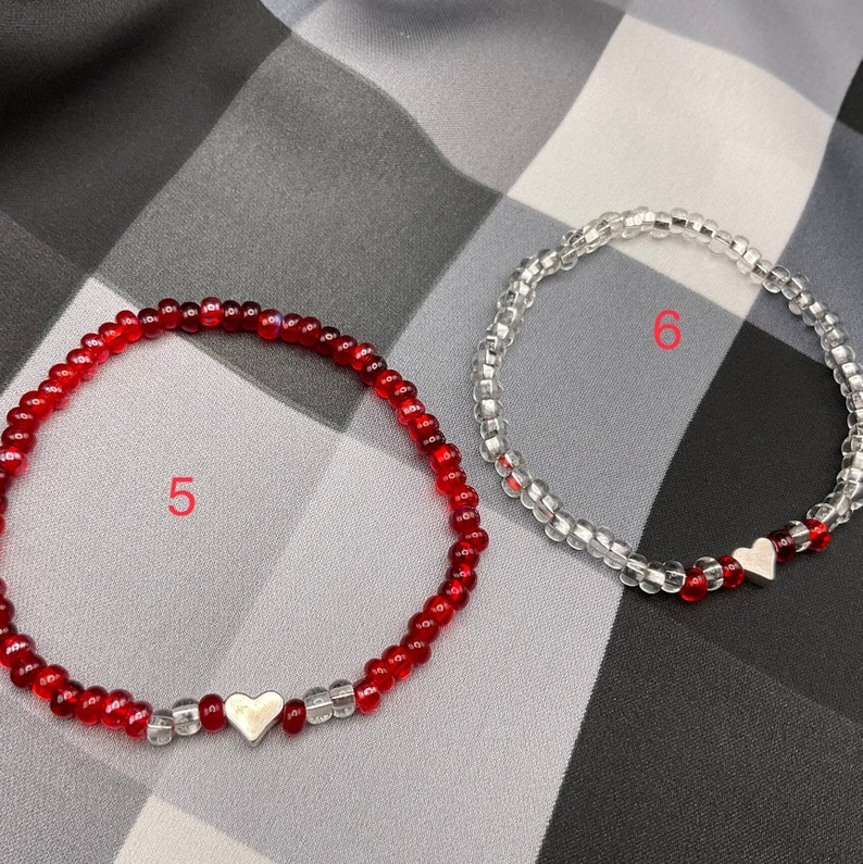May include: Two beaded bracelets with silver heart charms. One bracelet is red and the other is clear.
