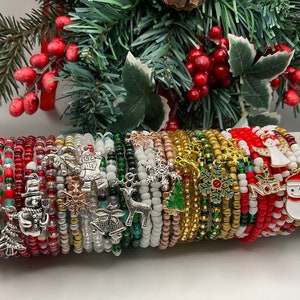 May include: A set of colorful Christmas themed bracelets with various charms, including a snowman, a bell, a snowflake, a reindeer, and a Santa Claus. The bracelets are made of beads and are stacked on top of each other.