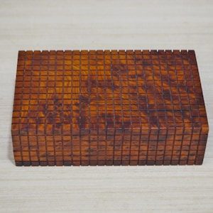 Peut inclure: Une boîte rectangulaire en bois avec un motif en damier. La boîte est en bois foncé avec une teinte brun rougeâtre.