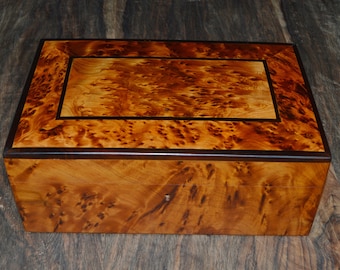 May include: A wooden box with a dark brown wood trim and a light brown wood interior. The box has a unique wood grain pattern.