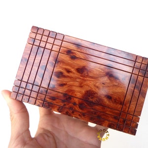 Könnte beinhalten: Eine rechteckige Holzkiste mit einem dekorativen, komplizierten Design. Die Kiste ist aus dunkelrotem Holz mit einem natürlichen Holzmaserungsmuster. Die Kiste hat einen erhöhten Rand um die Kanten und ein kleineres, erhöhtes Rechteck in der Mitte.