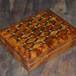 Op de afbeelding: Een houten doos met een geometrisch patroon ingelegd met goud en parelmoer. De doos heeft een scharnierend deksel en is gemaakt van een rijk bruin hout.