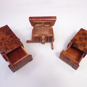 Puede incluir: Tres cajas de madera en tonos marrón rojizo. Una caja está abierta, mostrando su interior, mientras que las otras dos tienen sus cajones extendidos. La caja central tiene una tapa con bisagras y una pequeña cerradura.