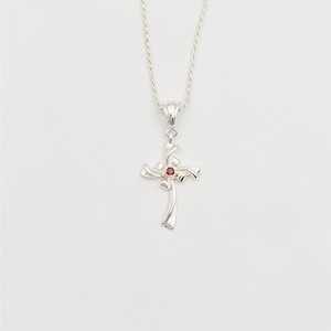 May include: Silver necklace with a red gemstone cross pendant. The cross is a stylized design with a swirl pattern.