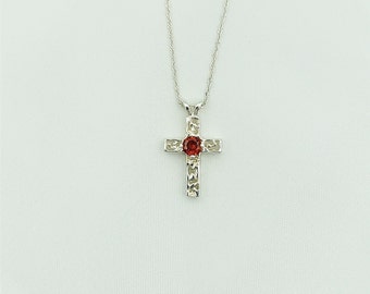 Puede incluir: Collar de plata con un colgante de cruz con una piedra roja.