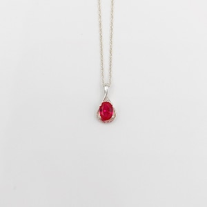 May include: A silver chain necklace with a red oval gemstone pendant set in a silver filigree design.