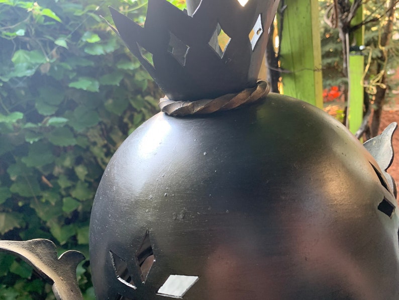 K&ouml;nnte beinhalten: Eine schwarze Metallsculptur einer Krone auf einer Kugel mit ausgeschnittenen Diamantenformen. Die Kugel steht auf einem Metallsockel.