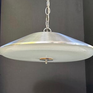 May include: A vintage pendant light with a silver metal shade and a frosted glass diffuser. The light fitting is suspended from a silver chain. The shade has a diameter of approximately 40 cm.