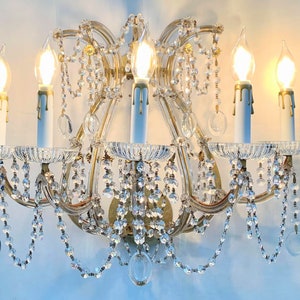 May include: A gold-toned crystal wall sconce with five candle-style light bulbs. The sconce features a cascading design with crystal beads and teardrop-shaped crystals.