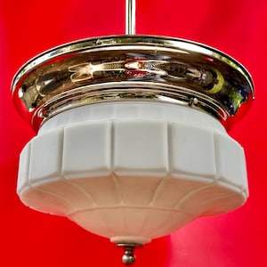 May include: A vintage ceiling light fixture with a polished chrome top and a white, geometric-shaped glass shade. The fixture hangs from a silver rod against a vibrant red background. The shade has a rounded bottom with a small, decorative metal ball.