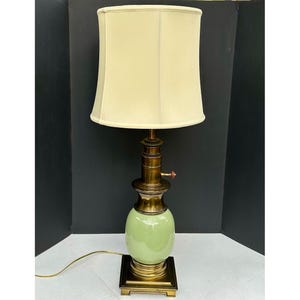 May include: A vintage table lamp with a pale green ceramic base and brass accents. The lamp features a cream-colored lampshade and a square brass base. The lamp is approximately 28 inches tall.