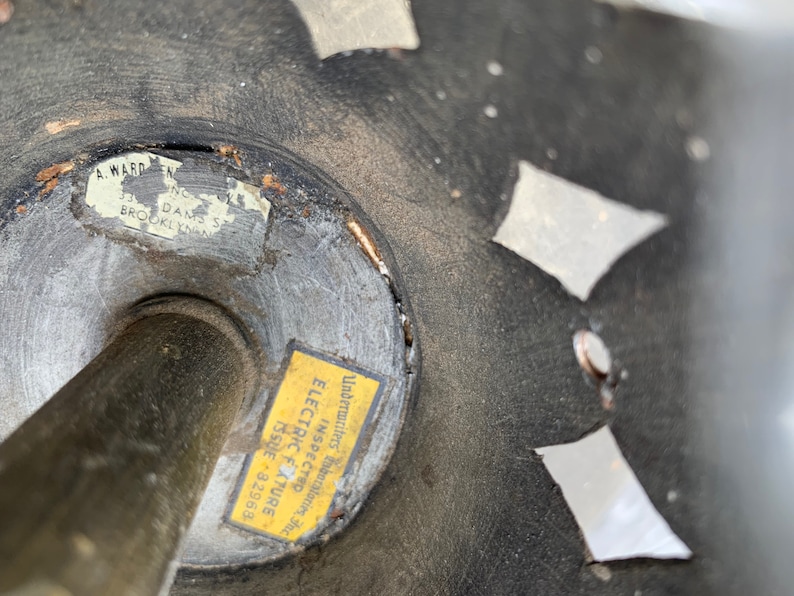 K&ouml;nnte beinhalten: Nahaufnahme einer schwarzen Metallleuchte mit einem dekorativen Design. Ein gelber Aufkleber mit dem Text "Underwriters' Laboratories Inc. Electric Fixture Inspected Issue 82968" ist an der Leuchte angebracht.