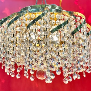 May include: A gold chandelier with crystal drops hanging from the bottom. The chandelier has a circular shape and is made of metal.