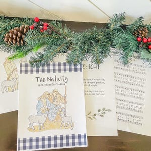 May include: A black and white checkered book with the title "The Nativity: A Christmas Eve Tradition". The book features a hand-drawn illustration of the nativity scene with Mary, Joseph, and baby Jesus in a manger with two sheep.