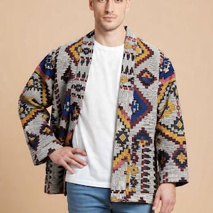 Peut inclure: Veste à motifs avec un motif géométrique dans les tons de gris, jaune, bleu et rouge. La veste est ouverte, révélant un t-shirt blanc. La personne porte un jean bleu.