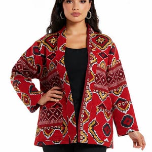 Peut inclure: Veste rouge à motifs géométriques jaunes, blancs et noirs. La veste a un col châle et une fermeture boutonnée. La veste est portée sur un haut noir et un pantalon noir. La veste est de longueur moyenne.