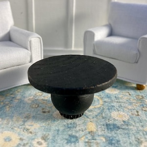 May include: A black round coffee table with a smooth, wooden top and a round, black base. The table is sitting on a blue and white patterned rug.