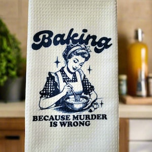 May include: A white kitchen towel with a blue illustration of a woman baking. The text "Baking because murder is wrong" is printed on the towel.