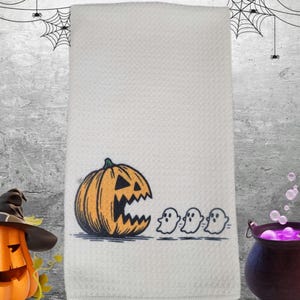 May include: White Halloween-themed hand towel featuring an orange jack-o'-lantern with a black outline and three small white ghosts. The towel has a textured pattern and is perfect for seasonal decor.