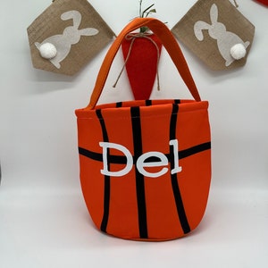 May include: Orange and black basketball-themed Easter basket with the name "Del" printed in white on the front.