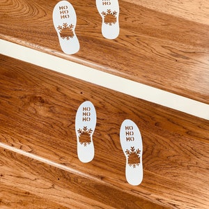 May include: Four white footprints with the words "HO HO HO" and a snowflake design on a wooden staircase.