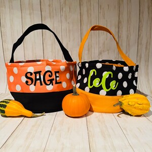 May include: Two orange and black Halloween trick-or-treat bags with white polka dots. The bags have black handles and are personalized with the names "Sage" and "LeLe" in green letters.
