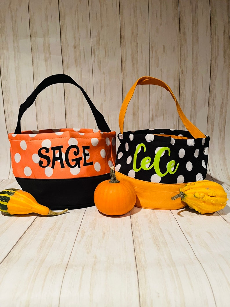 May include: Two orange and black Halloween trick-or-treat bags with white polka dots. The bags have black handles and are personalized with the names "Sage" and "LeLe" in green letters.