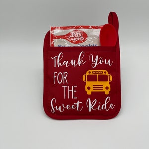 Puede incluir: Manopla de horno roja con el texto "Thank You For The Sweet Ride" y un gr&aacute;fico de autob&uacute;s escolar amarillo. Una peque&ntilde;a cuchara roja y un paquete de galletas de az&uacute;car Betty Crocker est&aacute;n dentro de la manopla.