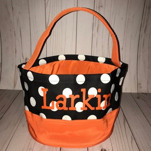 May include: Orange and black polka dot trick or treat bag with the name Larkin embroidered in orange on the front.