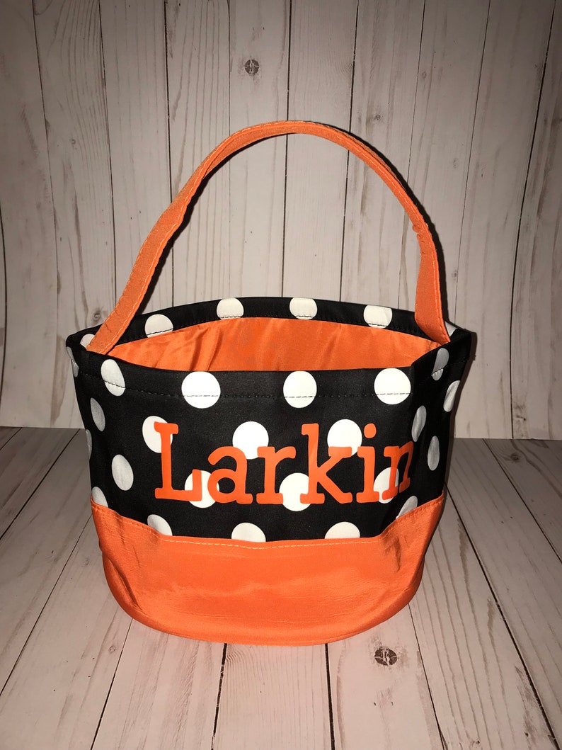 May include: Orange and black polka dot trick or treat bag with the name Larkin embroidered in orange on the front.